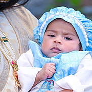 Samrat is registered to the contest to win money with this photo: baby, infant, child, portrait, blue_bonnet, white_clothing, adult, parent, holding, arms, face, eyes, indoor, traditional_clothing, jewelry, necklace, headwear, closeup, photography, family