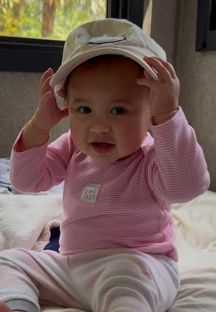 Reese is registered to the contest to win money with this photo: baby, child, hat, pink_clothing, striped, indoor, blanket, window, cute, smiling, face, hands, sitting, infant, cozy, soft_lighting, portrait, person, cute_baby, playful