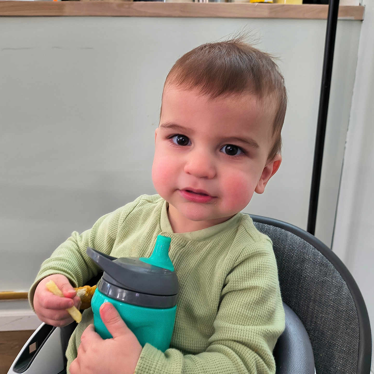 Issac joined the competition — help win amazing prizes! toddler, child, sippy_cup, high_chair, indoor, kitchen, jars, gloves, green_sweater, curly_hair, cute, rosy_cheeks, person, seated, holding, food, snack, expression, face, young_child