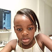 Tiana participe au concours pour gagner de l'argent avec cette photo : child, portrait, indoor, tank_top, necklace, hairstyle, face, person, young, thoughtful, brown_skin, casual_clothing, living_room, television, blurred_background, furniture, home, closeup, skin, expression