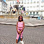 accessory, buildings, casual_clothing, child, cobblestone, daylight, fashion, fountain, girl, outdoor, person, pink_outfit, smiling, square, standing, statue, sunglasses, sunny, urban, youth
