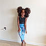 Tiana participe au concours pour gagner de l'argent avec cette photo : child, girl, standing, barefoot, black_top, blue_pants, butterfly_patches, curly_hair, puffy_hair, indoor, wooden_floor, minimalist_background, pose, smile, casual_clothing, playful, young, person, portrait, natural_light
