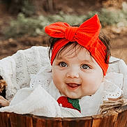 Aria is registered to the contest to win money with this photo: baby, infant, headband, red_bow, wooden_bucket, blanket, smiling, outdoor, nature, cute, portrait, child, face, happy, soft_light, clothing, young, sitting, expression, closeup