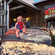 Caysen is registered to the contest to win money with this photo: baby, child, toddler, superhero_costume, spiderman, sitting, vintage_truck, truck_hood, rusty_vehicle, weathered_paint, rustic_building, wooden_building, outdoor, sunny, blue_sky, portrait, facial_expression, blonde_hair, automotive, nostalgic
