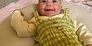 Bonnie is registered to the contest to win money with this photo: baby, blanket, checkered_pattern, child, clothing, comfortable, cushion, cute, face, green_dress, happy, head, indoor, infant, lying_down, person, portrait, skin, smiling, soft_texture