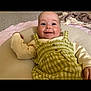 Bonnie is registered to the contest to win money with this photo: baby, smiling, infant, cushion, green_dress, checkered_pattern, blanket, indoor, happy, child, face, cute, comfortable, clothing, person, portrait, lying_down, soft_texture, head, skin