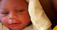 Jakai is registered to the contest to win money with this photo: baby, bundled_up, carrier, child, close_up, cozy, cute, eyes_open, face, indoor, infant, looking_at_camera, mittens, newborn, onesie, photograph, portrait, seated, striped_hat, warm_lighting