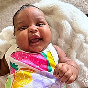 Londyn is registered to the contest to win money with this photo: baby, infant, smiling, colorful_clothing, fruit_pattern, blanket, soft_texture, happy, cute, portrait, child, hand, skin, face, expression, lying_down, indoors, comfort, warmth, closeup