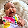baby, infant, smiling, colorful_clothing, fruit_pattern, blanket, soft_texture, happy, cute, portrait, child, hand, skin, face, expression, lying_down, indoors, comfort, warmth, closeup