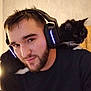 Flèche participe au concours pour gagner de l'argent avec cette photo : man, headphones, cat, black_cat, beard, indoor, shoulder_pet, smiling, young_adult, casual_clothing, technology, pet, companion, cozy, portrait, feline, relaxed, warm_lighting, human, indoor_lighting