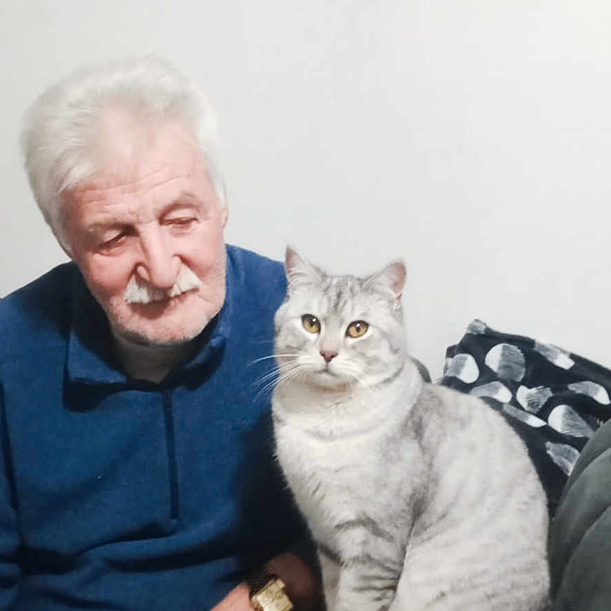 Duman Bir participe au concours pour gagner de l'argent avec cette photo : animal, blue_sweater, cat, companion, couch, decorative_wall_art, domestic, elderly_man, furniture, gray_cat, human, indoor, pet, portrait, relaxed, ring, seated, wall_clock, watch, white_hair