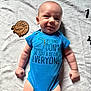 baby, infant, blue_onesie, smiling, dinosaur, wooden_cutout, blanket, pattern, two_months, cute, lying_down, child, happy, skin, head, face, arms, legs, indoors, closeup