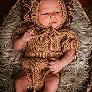 Calum joined the competition — help win amazing prizes! baby, infant, knitted_clothing, lion_costume, basket, fur_blanket, cozy, portrait, cute, soft_lighting, indoors, newborn, baby_legs, baby_hands, headgear, warm_colors, relaxed, child, person, closeup