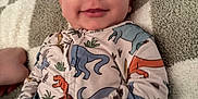 Calum joined the competition — help win amazing prizes! baby, infant, smiling, pajamas, dinosaur_print, blanket, fabric, hand, face, cute, sleepwear, lying_down, child, soft_texture, cozy, indoors, portrait, closeup, skin, head