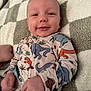 baby, infant, smiling, pajamas, dinosaur_print, blanket, fabric, hand, face, cute, sleepwear, lying_down, child, soft_texture, cozy, indoors, portrait, closeup, skin, head