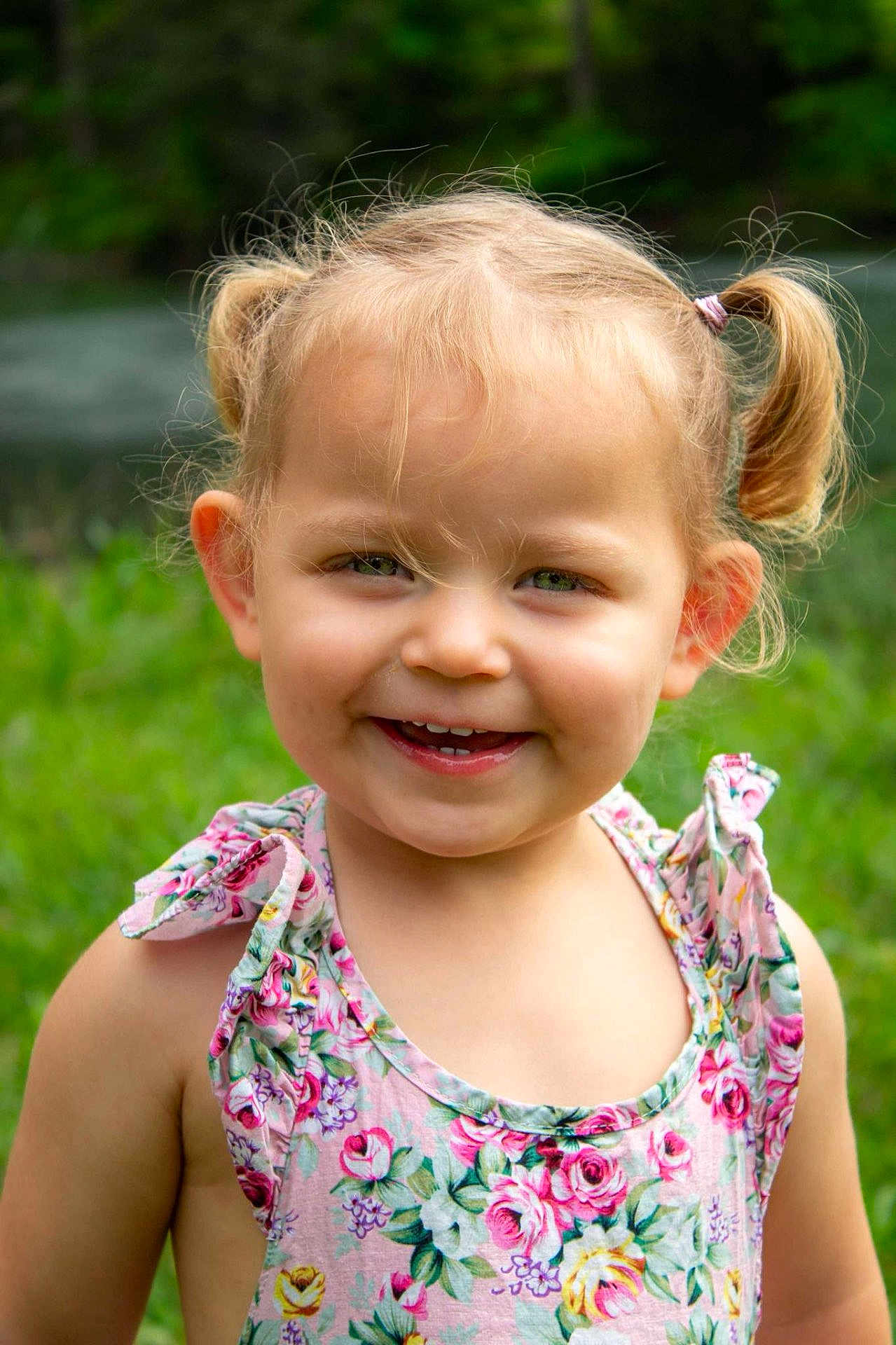 Bella is registered to the contest to win money with this photo: child, toddler, smiling, pigtails, blonde_hair, green_eyes, floral_dress, outdoor, nature, grass, summer, portrait, happy, cute, person, fashion, sunlight, closeup, face, young