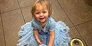 Bella joined the competition — help win amazing prizes! toddler, child, balloon, blue_dress, smiling, floor, tile, indoor, person, hand, face, hair, footwear, drain, light, shadow, clothing, happy, sitting, play