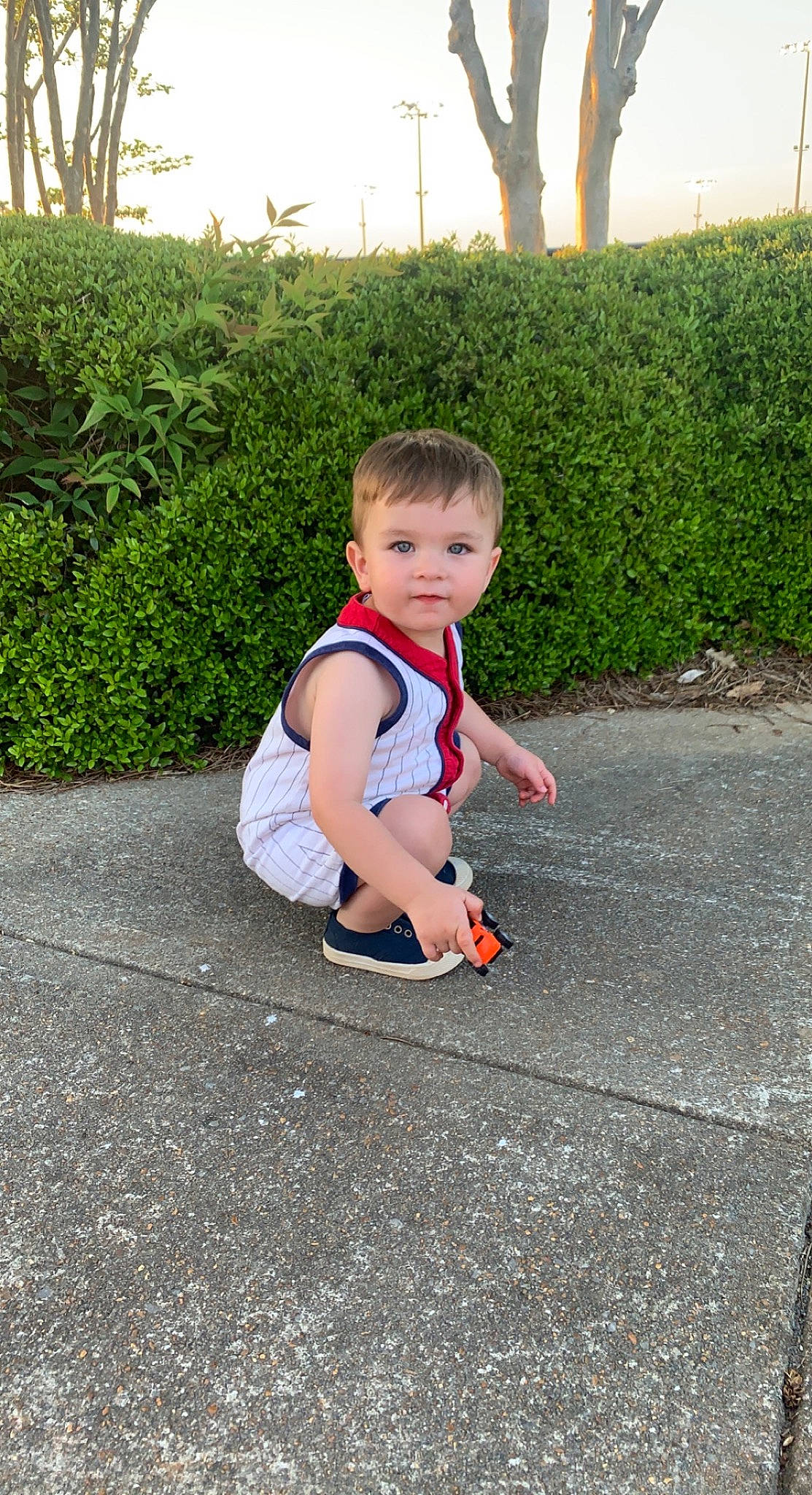 Landon is registered to the contest to win money with this photo: asphalt, baby, baby_toddler_clothing, flooring, fun, grass, hedge, lawn, leisure, people_in_nature, person, plant, recreation, road, road_surface, shrub, sidewalk, sitting, t_shirt, toddler