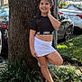 child, girl, smiling, braids, tree, outdoor, daylight, sporty_clothing, skirt, sneakers, greenery, plants, car, parking, nature, sunlight, happy, posing, casual, young