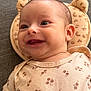baby, smiling, infant, onesie, floral_pattern, cushion, bear_shape, cute, happy, face, head, skin, clothing, lying_down, indoors, texture, fabric, closeup, child, person