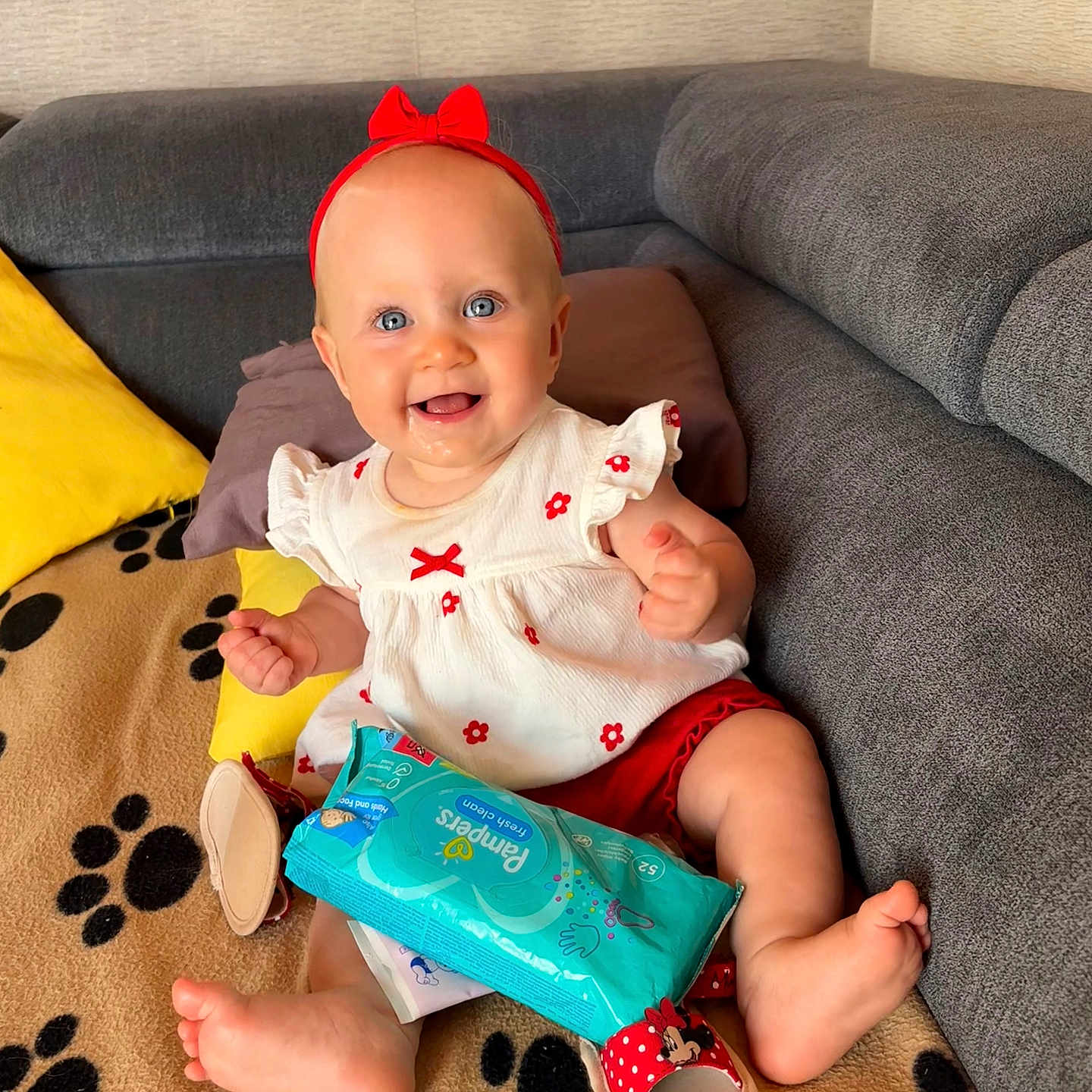Lou a rejoint le concours — aidez-le/la à gagner de superbes lots ! baby, blanket, blue_eyes, child, couch, cute, footwear, happy, headband, indoors, infant, minnie_mouse_sandals, pampers_wipes, paw_prints, pillows, red_bow, red_shorts, sitting, smiling, white_dress