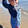 Amaël participe au concours pour gagner de l'argent avec cette photo : toddler, child, pacifier, denim_overalls, beach, ocean, sand, blue_sky, adult_hands, barefoot, casual_clothing, sunlight, smiling, outdoors, water, footwear, person, holding_hands, playful, summer