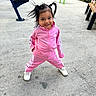 child, girl, pink_tracksuit, pigtails, smiling, outdoor, park, concrete, exercise_equipment, bench, shoes, casual_clothing, playful_pose, happy, person, daylight, hair, young_child, sporty, active
