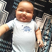 Phaylon is registered to the contest to win money with this photo: baby, infant, child, portrait, lying_down, tongue_out, playful, happy, face, smiling, onesie, dinosaur, blanket, patterned_blanket, indoor, close_up, five_months, tiktok_watermark, text_overlay, safe