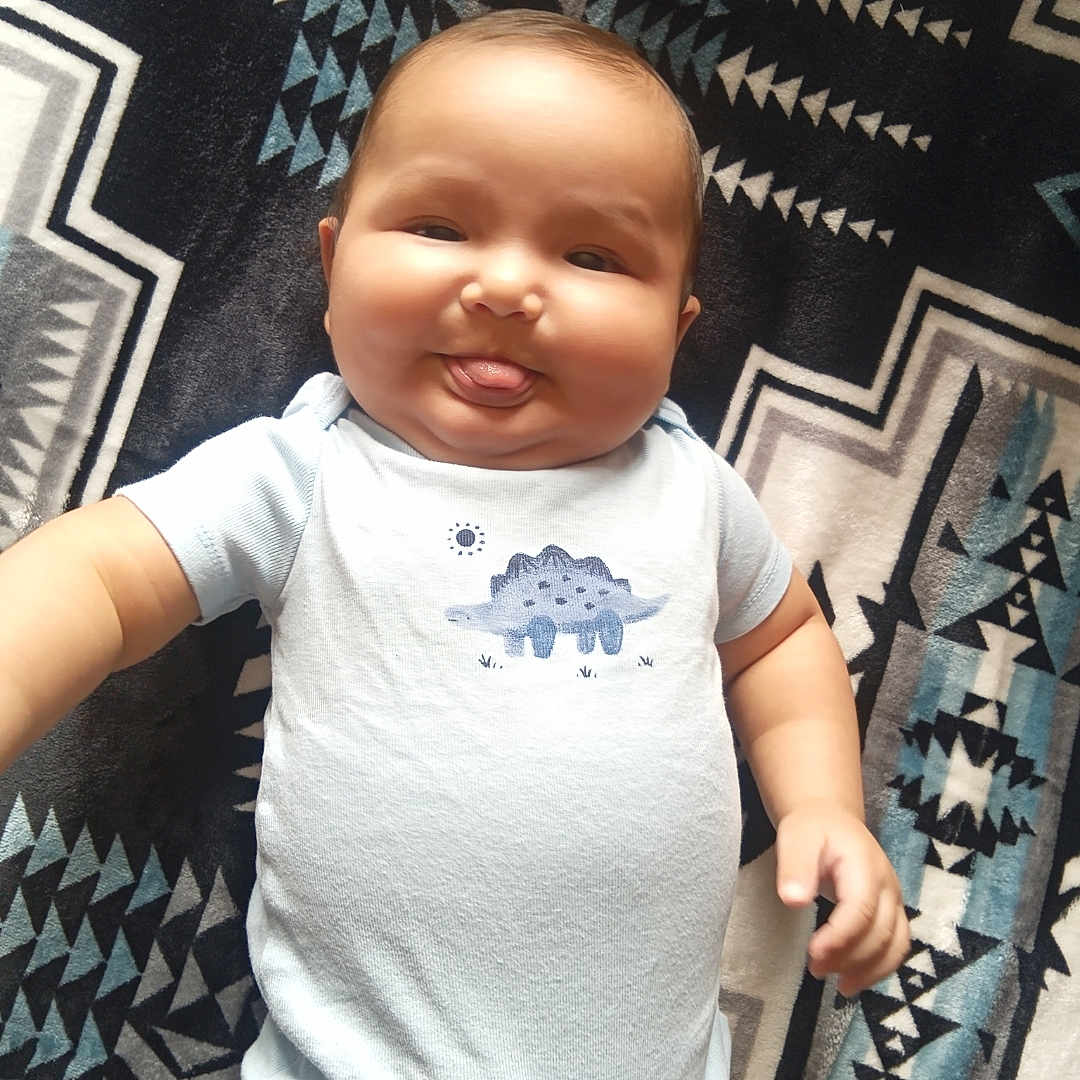 Phaylon is registered to the contest to win money with this photo: baby, infant, child, portrait, lying_down, tongue_out, playful, happy, face, smiling, onesie, dinosaur, blanket, patterned_blanket, indoor, close_up, five_months, tiktok_watermark, text_overlay, safe