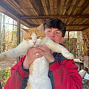 Gus joined the competition — help win amazing prizes! animal, background, casual, cat, daylight, expression, fall, feline, forest, holding, nature, outdoor, person, pet, red_jacket, relaxed, sunlight, wood, wooden_porch, young_adult