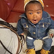 Millie joined the competition — help win amazing prizes! baby, child, denim_jacket, denim_jeans, beanie, boots, couch, leather, person, braids, hair, indoor, surprised_expression, sitting, clothing, casual, young_child, face, portrait, cozy