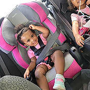 Vella joined the competition — help win amazing prizes! child, toddler, car_seat, seatbelt, smile, pink, black, sunglasses, hair_bun, shoe, clothing, car_interior, happy, cute, baby, seat, safety, playful, person, vehicle