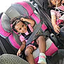 child, toddler, car_seat, seatbelt, smile, pink, black, sunglasses, hair_bun, shoe, clothing, car_interior, happy, cute, baby, seat, safety, playful, person, vehicle