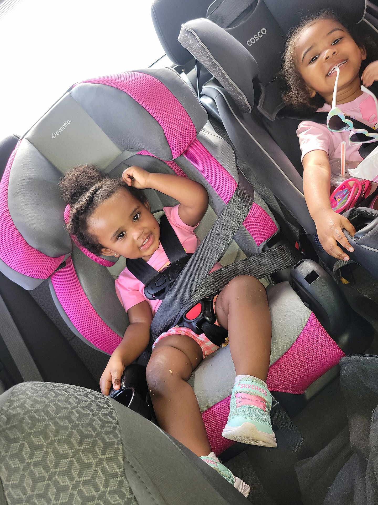 Vella joined the competition — help win amazing prizes! child, toddler, car_seat, seatbelt, smile, pink, black, sunglasses, hair_bun, shoe, clothing, car_interior, happy, cute, baby, seat, safety, playful, person, vehicle