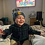 Zayden is registered to the contest to win money with this photo: toddler, child, hat, smiling, bed, plaid_shirt, laughing, indoor, television, cartoon, fan, guitar, furniture, room, cozy, clothing, pants, happy, person, home