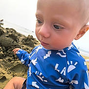 Léon participe au concours pour gagner de l'argent avec cette photo : baby, child, close_up, blue_clothing, beach, sand, outdoor, curious, bald_head, patterned_shirt, sea, summer, vacation, sunny, young_child, sitting, casual, daytime, nature, portrait