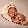 baby, newborn, sleeping, hat, pillow, blanket, soft_texture, peaceful, infant, resting, cute, portrait, cozy, warm_tones, skin, child, knitted_hat, pom_poms, flower, toddler