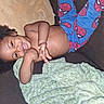 child, toddler, smiling, portrait, lying_down, indoor, pajamas, spiderman, blanket, pillow, floor, couch, curly_hair, brown_skin, happy, playful, reaching, front_view, casual, home