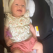 Stella participe au concours pour gagner de l'argent avec cette photo : baby, child, car_seat, headband, pacifier, plush_toy, smiling, clothing, pink_shorts, floral_top, infant, seat, sitting, cute, happy, indoor, toy, head, face, person