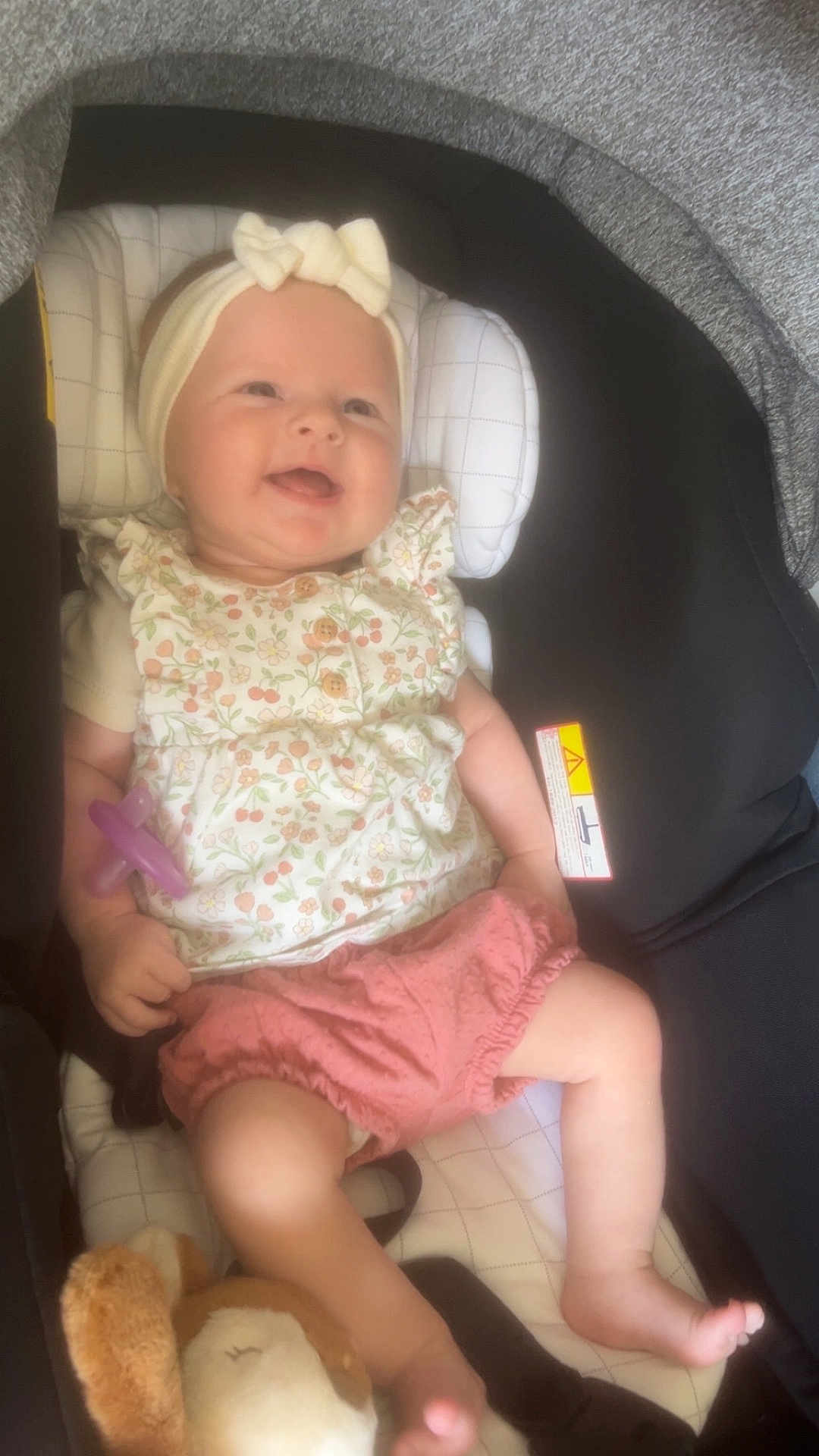 Stella participe au concours pour gagner de l'argent avec cette photo : baby, child, car_seat, headband, pacifier, plush_toy, smiling, clothing, pink_shorts, floral_top, infant, seat, sitting, cute, happy, indoor, toy, head, face, person