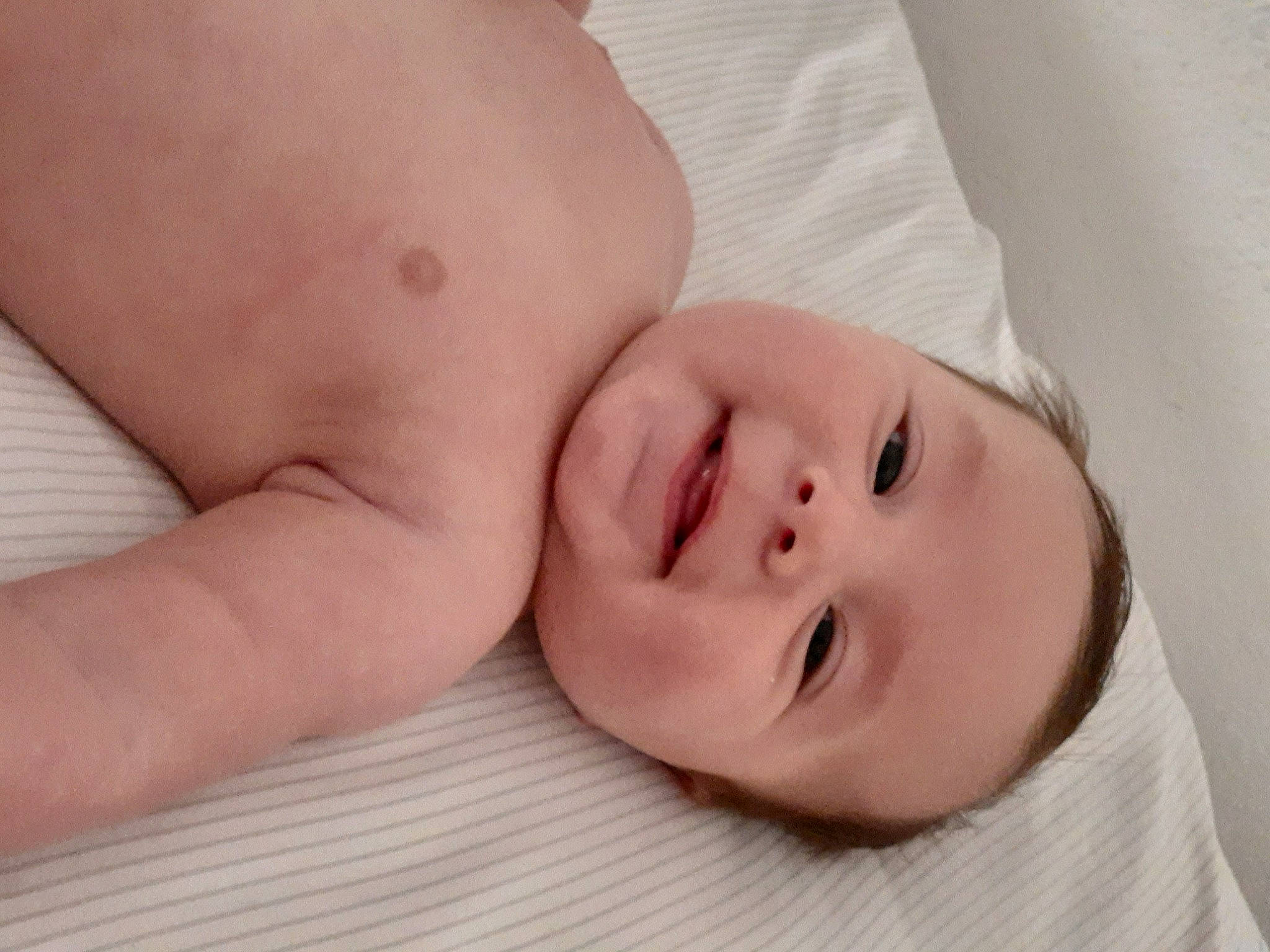 Derek is registered to the contest to win money with this photo: baby, baby_toddler_clothing, cheek, child, close_up, comfort, eye, eyebrow, gesture, happy, head, human_body, linens, lip, nose, person, skin, smile, stomach, thumb