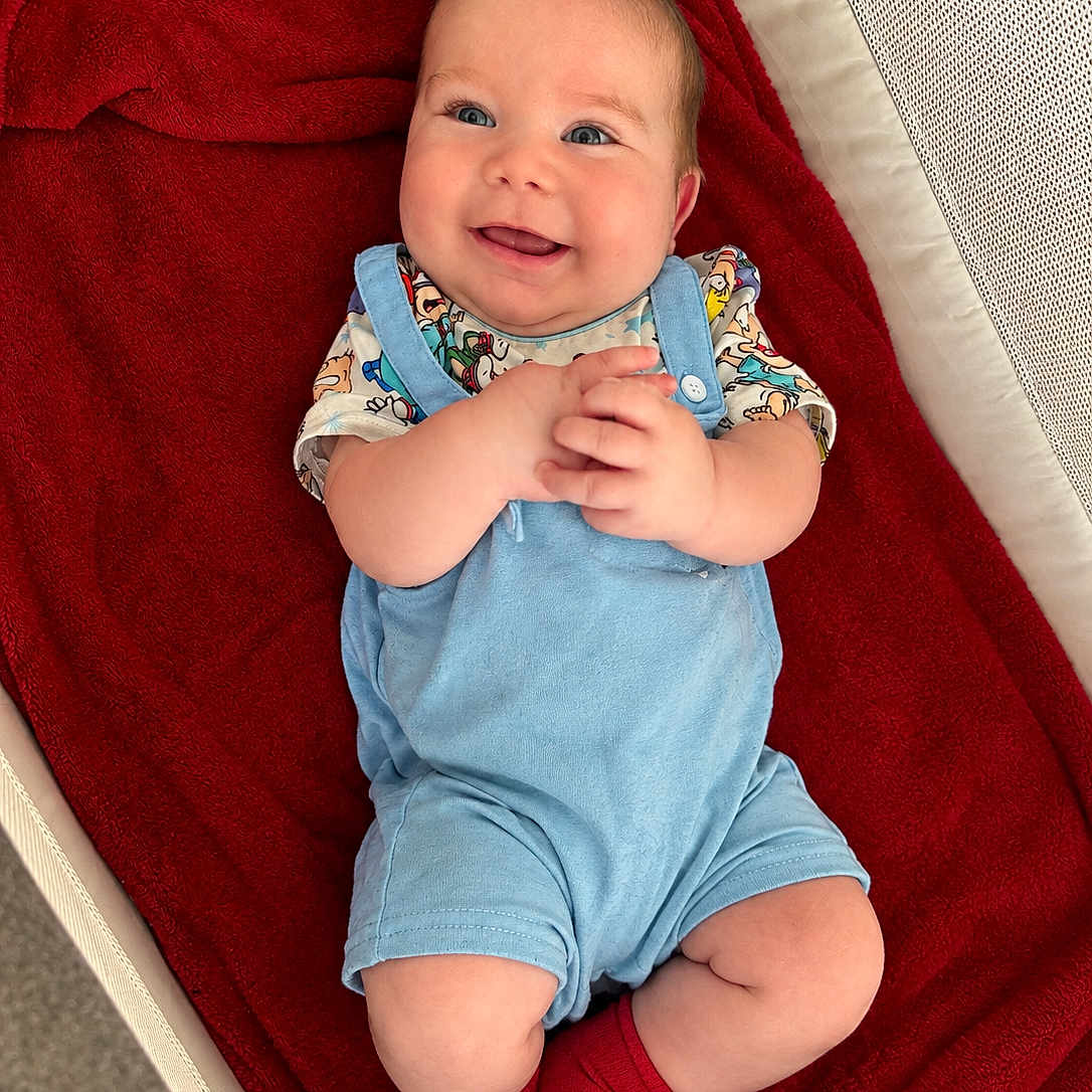 Kaysen joined the competition — help win amazing prizes! baby, child, infant, smiling, happy, portrait, lying_down, bassinet, blanket, red_blanket, blue_outfit, red_socks, colorful_clothing, baby_carriage, indoor, cozy, face, hands, feet, photography