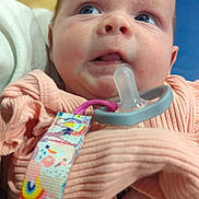 Emri is registered to the contest to win money with this photo: baby, infant, pacifier, clothing, closeup, indoor, person, blue_eyes, hand, fabric, cute, child, expression, soft_lighting, holding, colorful, pacifier_clip, skin, young, portrait