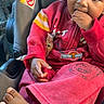 baby, child, infant, car_seat, vehicle, sitting, portrait, smiling, hand_to_mouth, red_clothing, striped_sleeves, barefoot, curly_hair, dark_skin, face, eyes, travel, indoors, close_up, happy