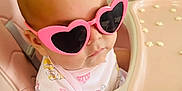 Vivian is registered to the contest to win money with this photo: baby, sunglasses, pink, heart_shaped, high_chair, infant, child, cute, fashion, apparel, person, indoor, seat, table, food, snack, portrait, playful, accessory, young