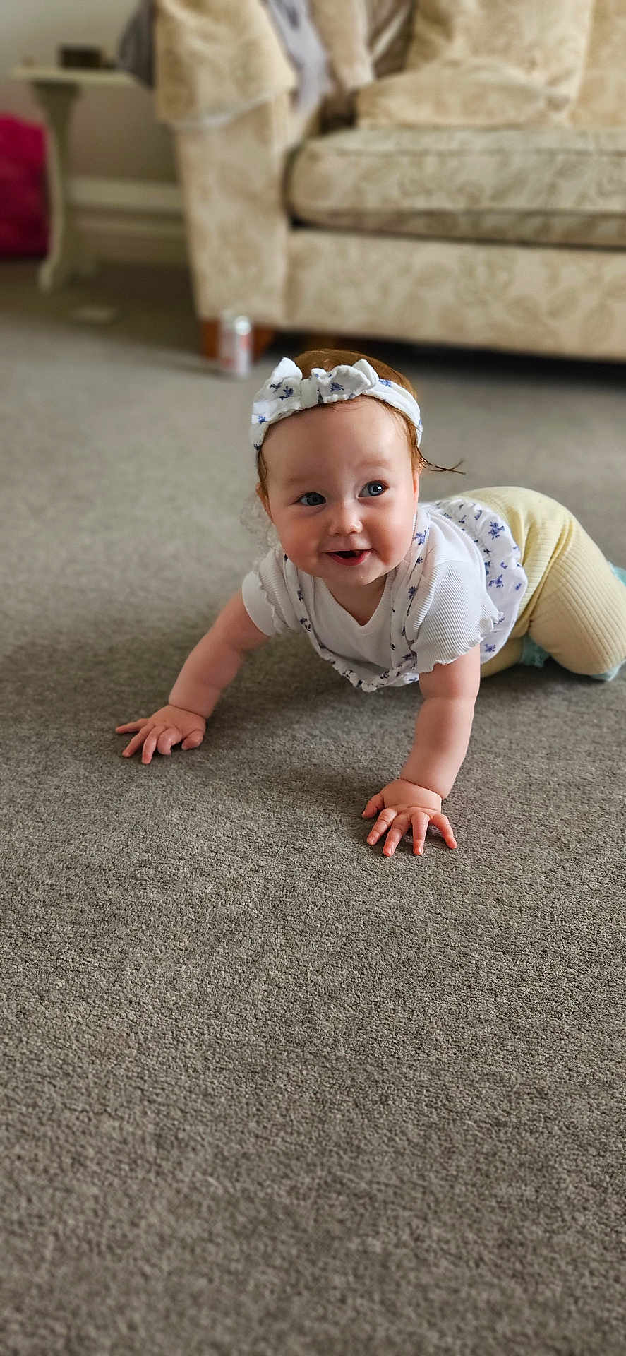 Freya joined the competition — help win amazing prizes! baby, carpet, casual_clothing, child, crawling, cute, floor, hands, happy, headband, home, indoor, living_room, person, portrait, smiling, sofa, white_top, yellow_pants, young_child