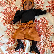 Julani joined the competition — help win amazing prizes! accessories, baby, black_shoes, black_top, blanket, bow, calm, child, clothing, coral_pattern, cute, fashion, fishnet_tights, hat, indoor, infant, lying_down, orange_skirt, patterned_background, portrait