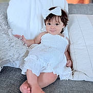 Anneli is registered to the contest to win money with this photo: baby, child, smiling, white_dress, headband, bow, couch, pillows, cozy, indoor, portrait, cute, infant, sitting, happy, relaxing, soft_lighting, homedecor, person, casual