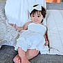 baby, child, smiling, white_dress, headband, bow, couch, pillows, cozy, indoor, portrait, cute, infant, sitting, happy, relaxing, soft_lighting, homedecor, person, casual