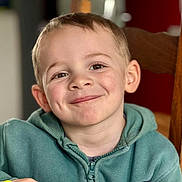 Mathys participe au concours pour gagner de l'argent avec cette photo : child, boy, smile, face, dimples, hoodie, green_clothing, chair, indoor, portrait, happy, casual, young, cute, person, head, seated, wood, background_blur, eyebrows
